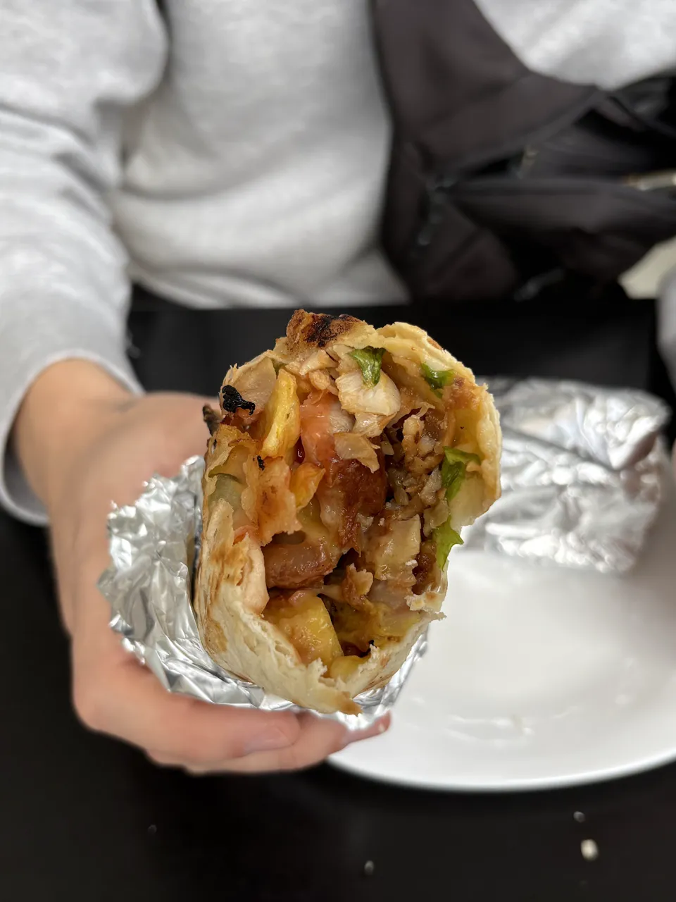 Shawarma in Alufolie in einer Hand, dahinter ein weißer Teller