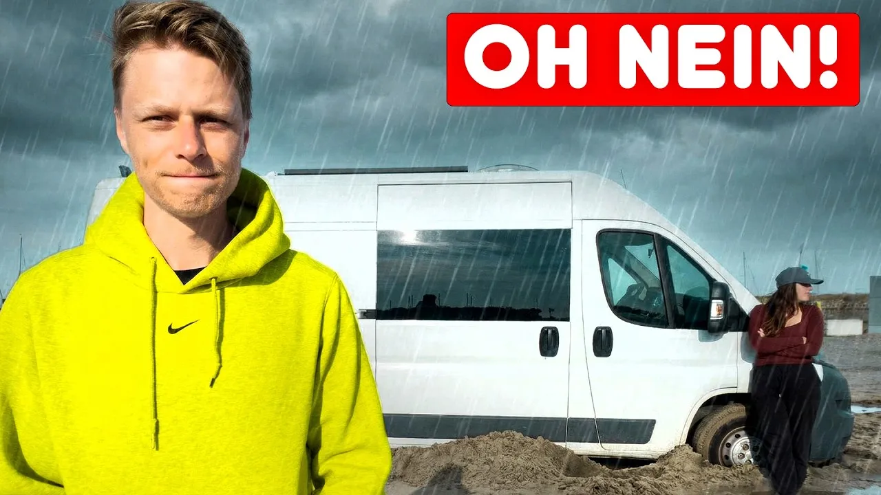 Titelbild unseres Videos „Oh nein“: Mark in gelbem Pullover vor unserem weißen Campervan, der im Regen im nassen Sand steht, daneben Lara