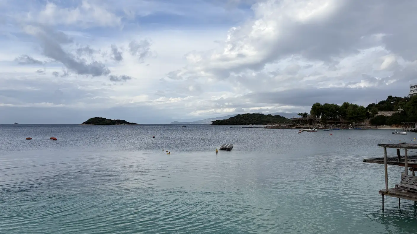 Ruhige Bucht bei Ksamil mit türkisem Wasser und kleinen Inseln vor der Küste unter Wolkenhimmel