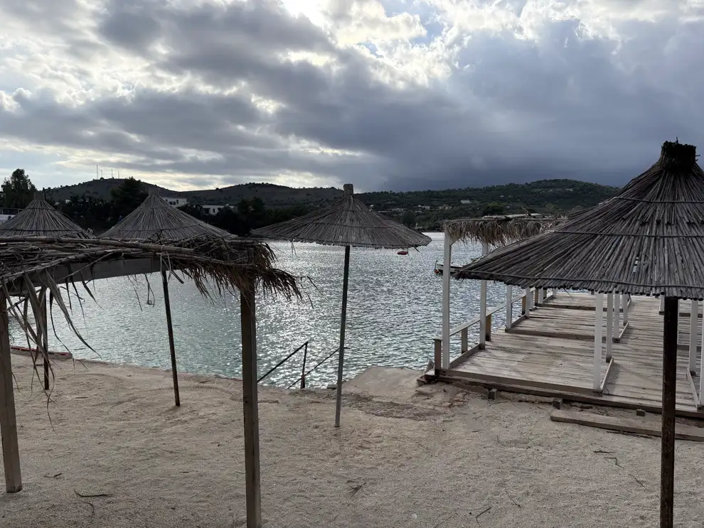 Leerer Holzsteg mit Strohschirmen am Strand von Ksamil in der Nebensaison