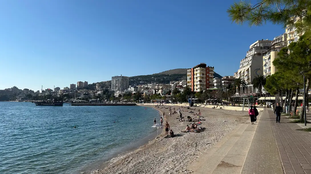 Promenade und Bucht von Saranda an der albanischen Riviera bei blauem Himmel, im Hintergrund die Stadt am Hang