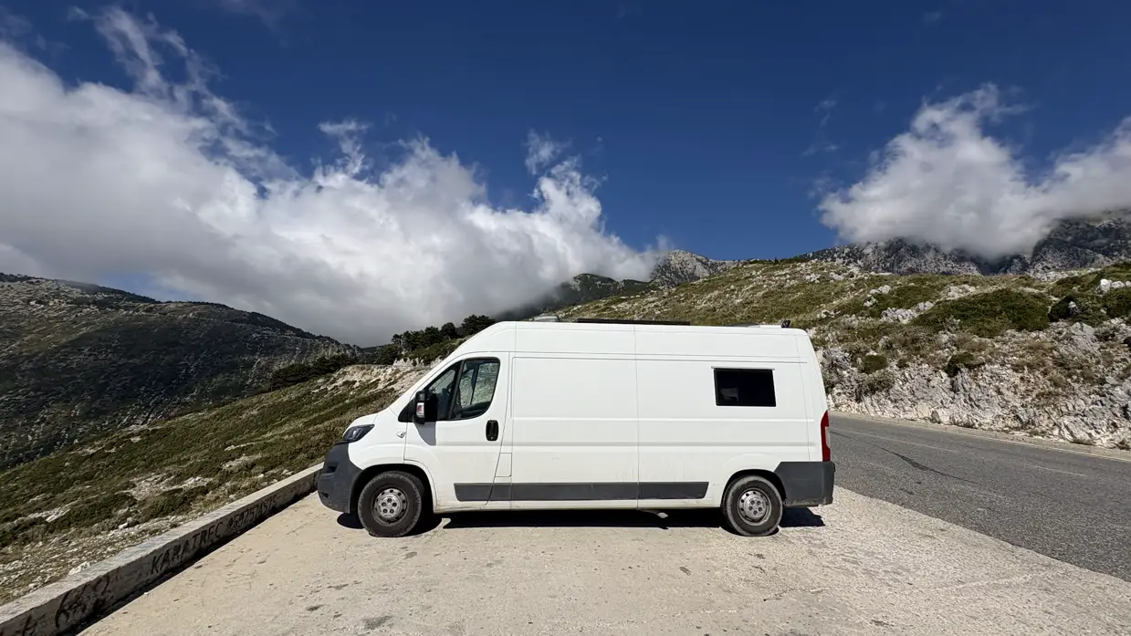 Unser weißer Kastenwagen an einem Aussichtspunkt am Llogara-Pass, dahinter felsige Berge und Wolken
