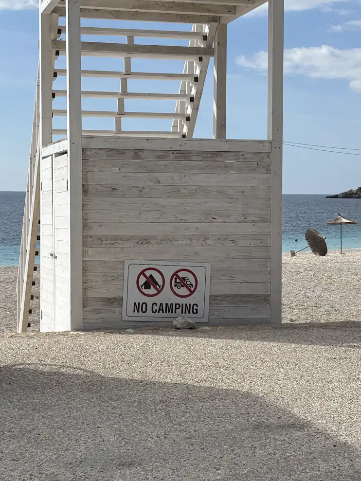 Schild „No camping“ an einem Rettungsschwimmerturm an einem Strand bei Himara an der albanischen Riviera