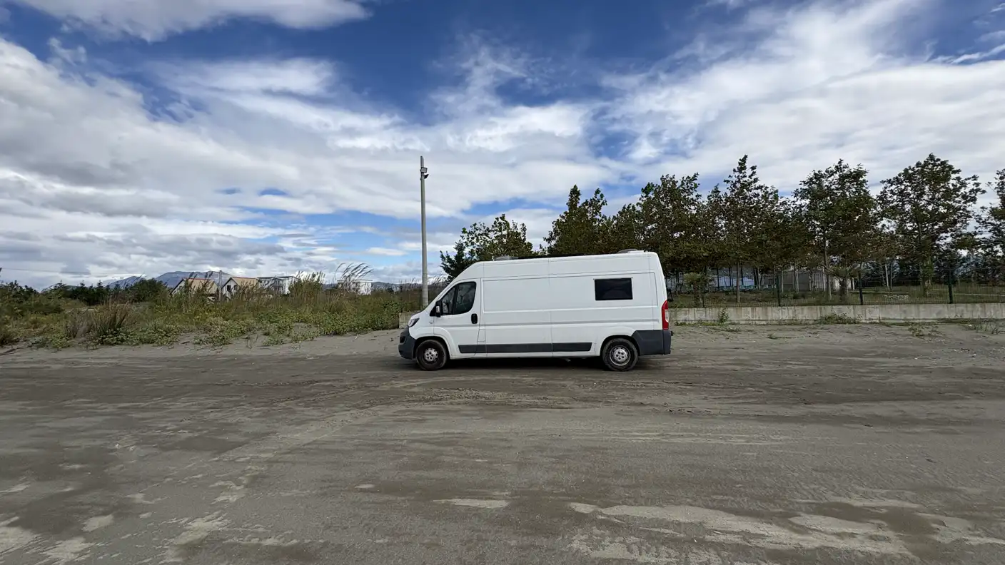 Unser weißer Campervan allein auf einer weiten Sandfläche unter Wolkenhimmel