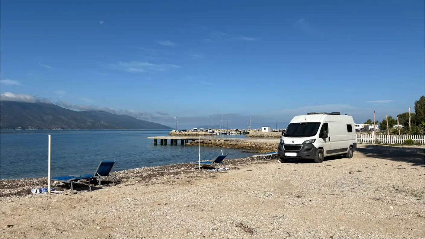 Unser weißer Campervan an einem Kiesstrand am Meer, davor blaue Sonnenliegen