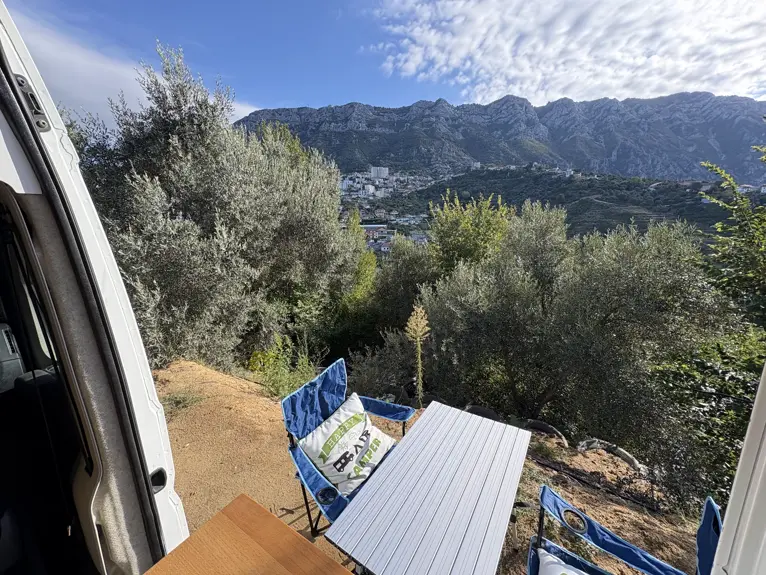 Blick vom Kruja Vista Camping über Olivenbäume auf die Stadt Kruja und die Berge, vorne Campingtisch und Stühle