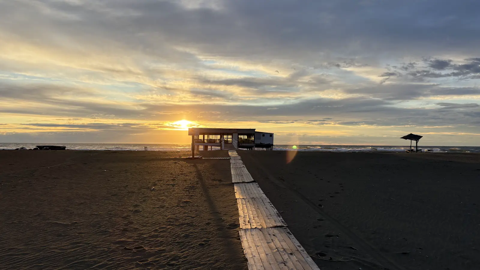 Sonnenuntergang an einem dunklen Sandstrand in Albanien mit Holzsteg und Strandhütte, unser Freisteh-Platz nach Shkodra