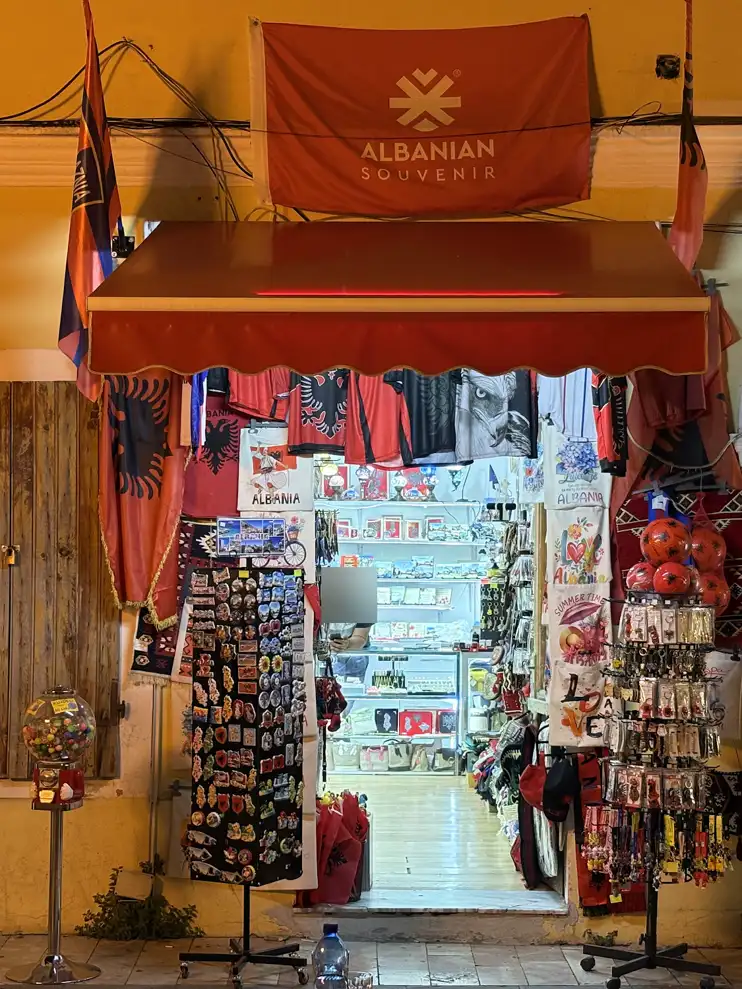 Souvenirladen in der Altstadt von Shkodra mit roten Albanien-Flaggen, Magneten und Taschen am Eingang