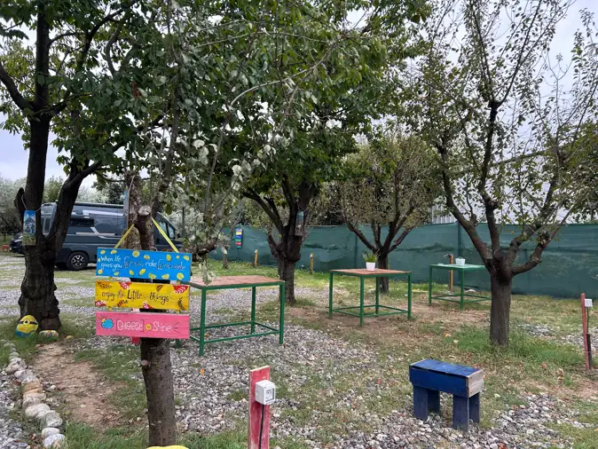 Parzellen auf Camping Bandula mit bunten Holzschildern, Tischen und Bäumen