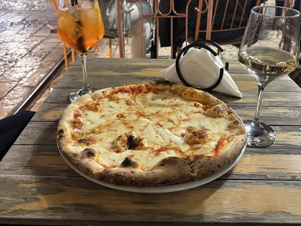 Pizza Margherita, Aperol Spritz und ein Glas Weißwein auf einem Holztisch im Restaurant Manifatura in Shkodra