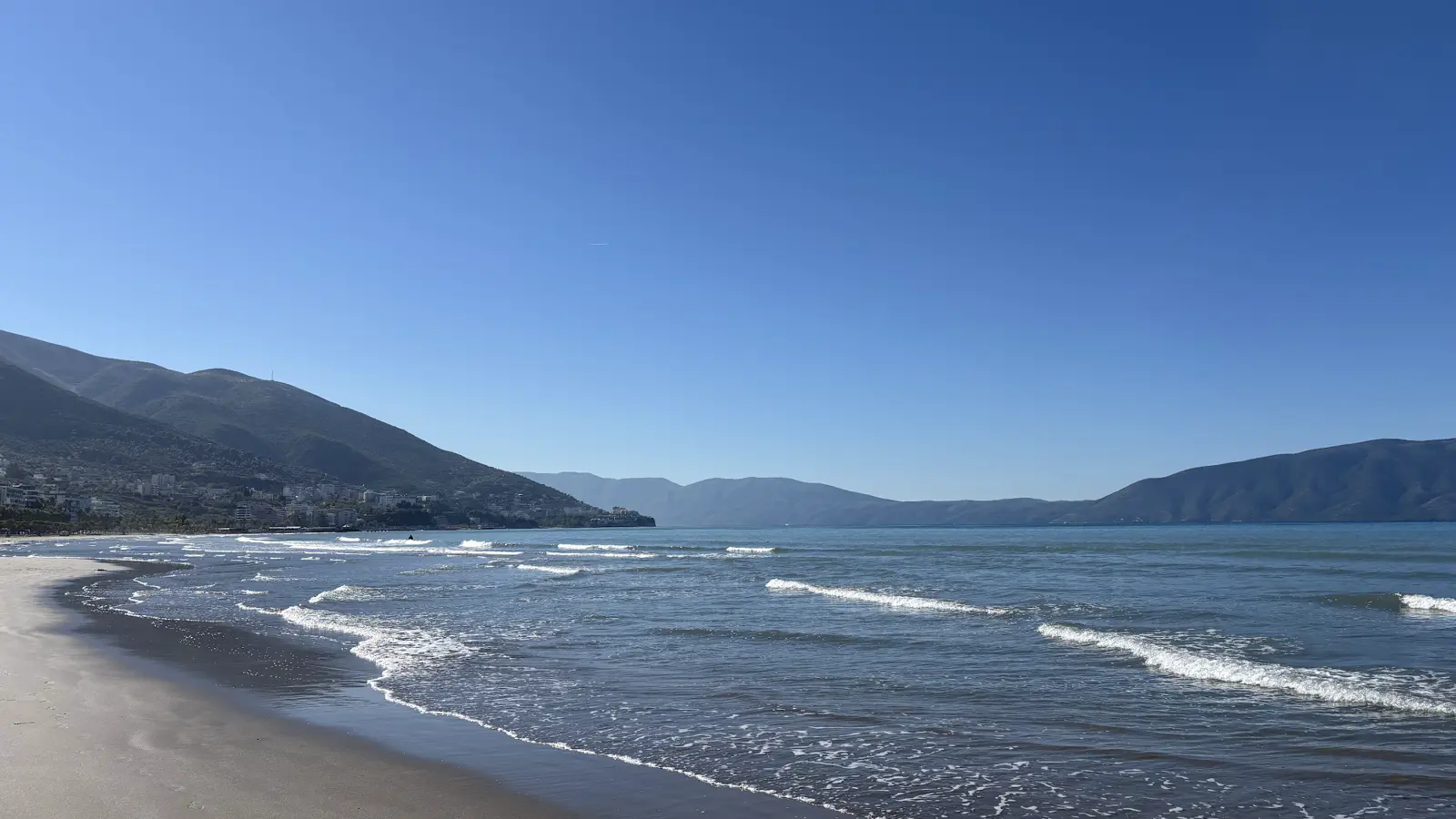 Strand von Vlora mit Wellen und der Bucht, im Hintergrund die Berge und die Stadt