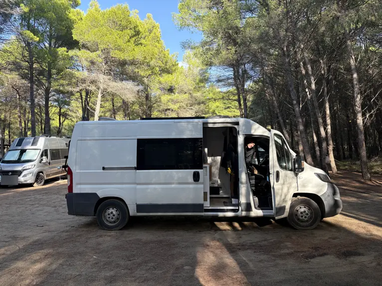 Unser Campervan mit offener Schiebetür im schattigen Kiefernwald des Eco Camping Valona