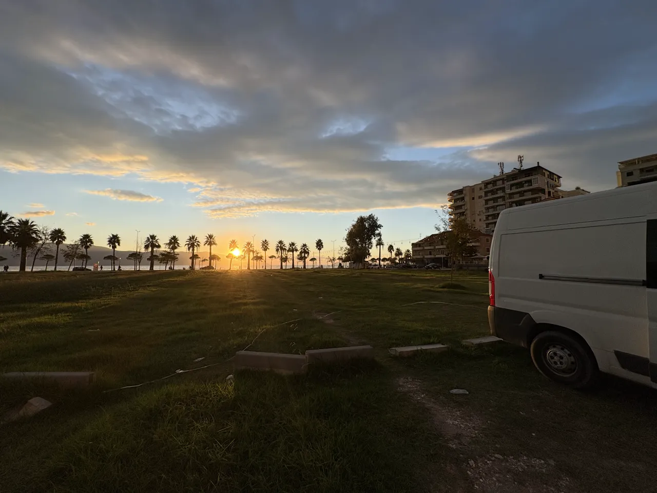 Sonnenuntergang zwischen Palmen am Meer in Vlora, rechts im Bild unser Camper