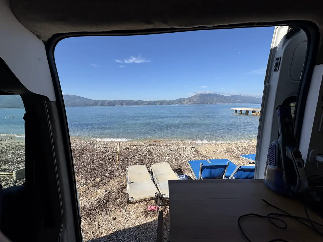 Blick aus der offenen Tür unseres Campers auf Sonnenliegen, Steg und die Bucht von Vlora