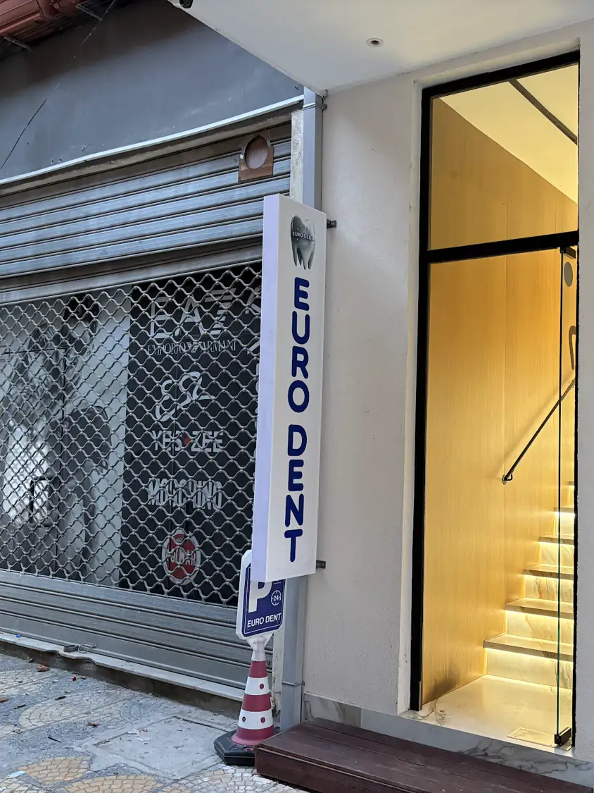 Eingang der Zahnarztpraxis Eurodent in Vlora mit senkrechtem Schild und beleuchteter Treppe