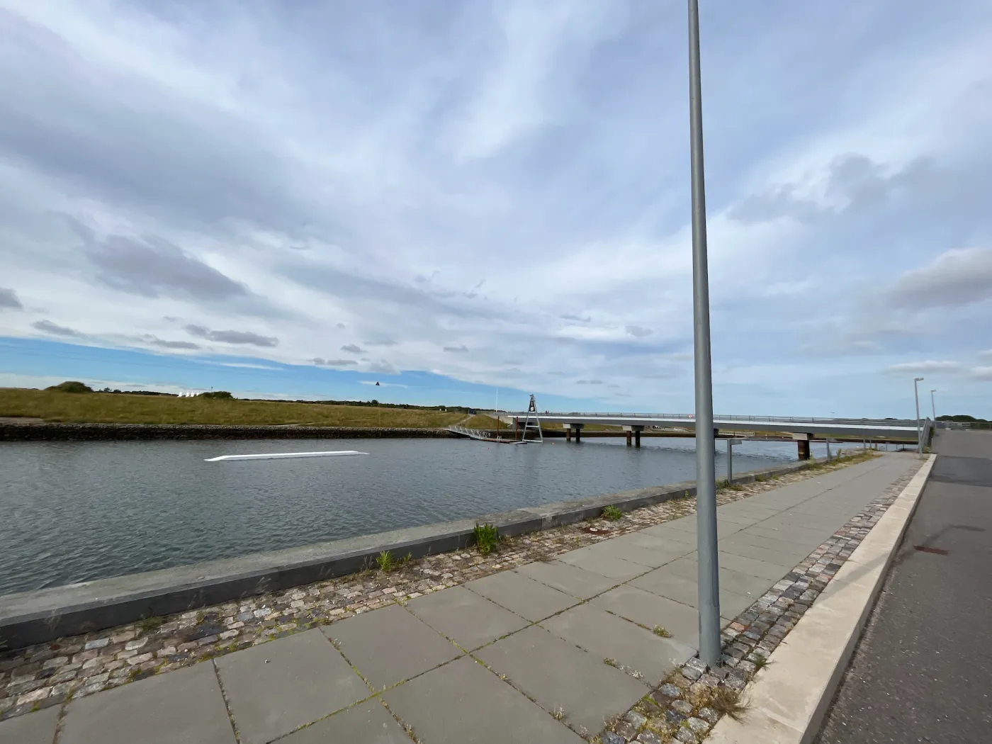 Kanal mit Badebereich und Fußgängerbrücke bei Esbjerg unter Wolkenhimmel
