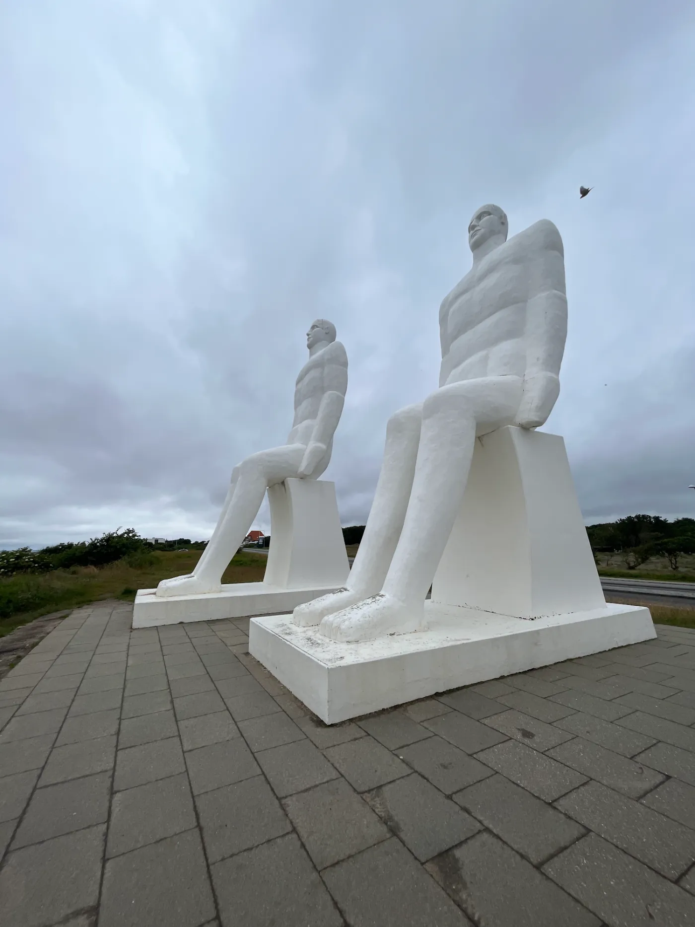 Zwei der neun Meter hohen weißen Betonfiguren von unten fotografiert vor bewölktem Himmel