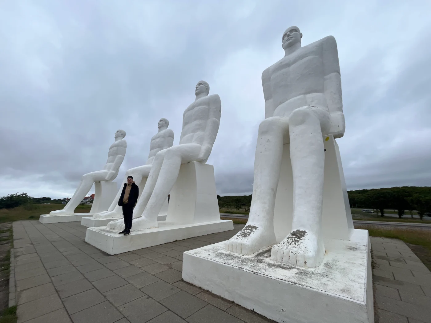 Vier weiße Sitzfiguren der Skulptur Der Mensch am Meer bei Esbjerg, davor Mark von Lehmann Vlogs als Größenvergleich