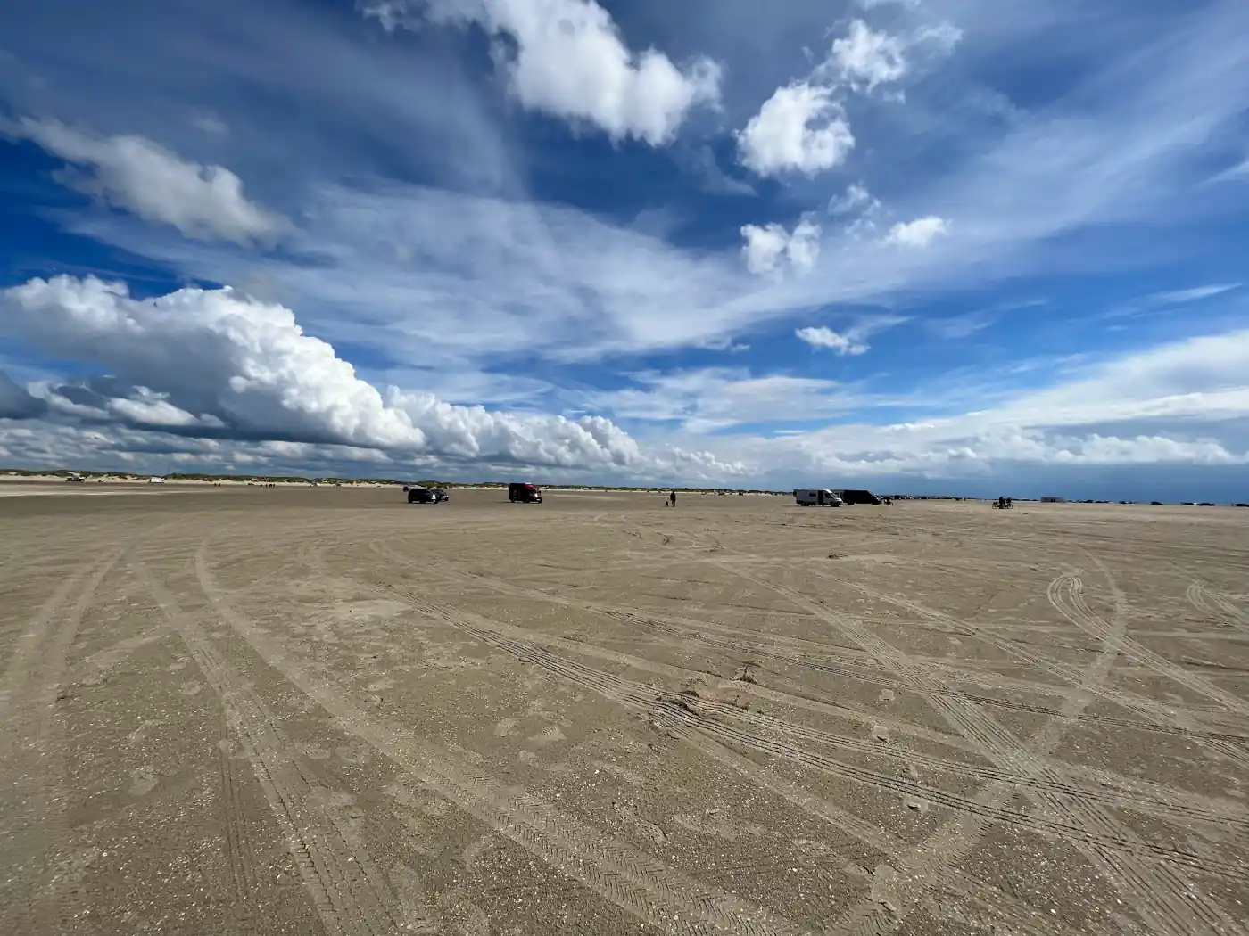 Weiter Sandstrand auf Rømø mit unzähligen Reifenspuren, einzelnen Fahrzeugen am Horizont und Wolkenhimmel