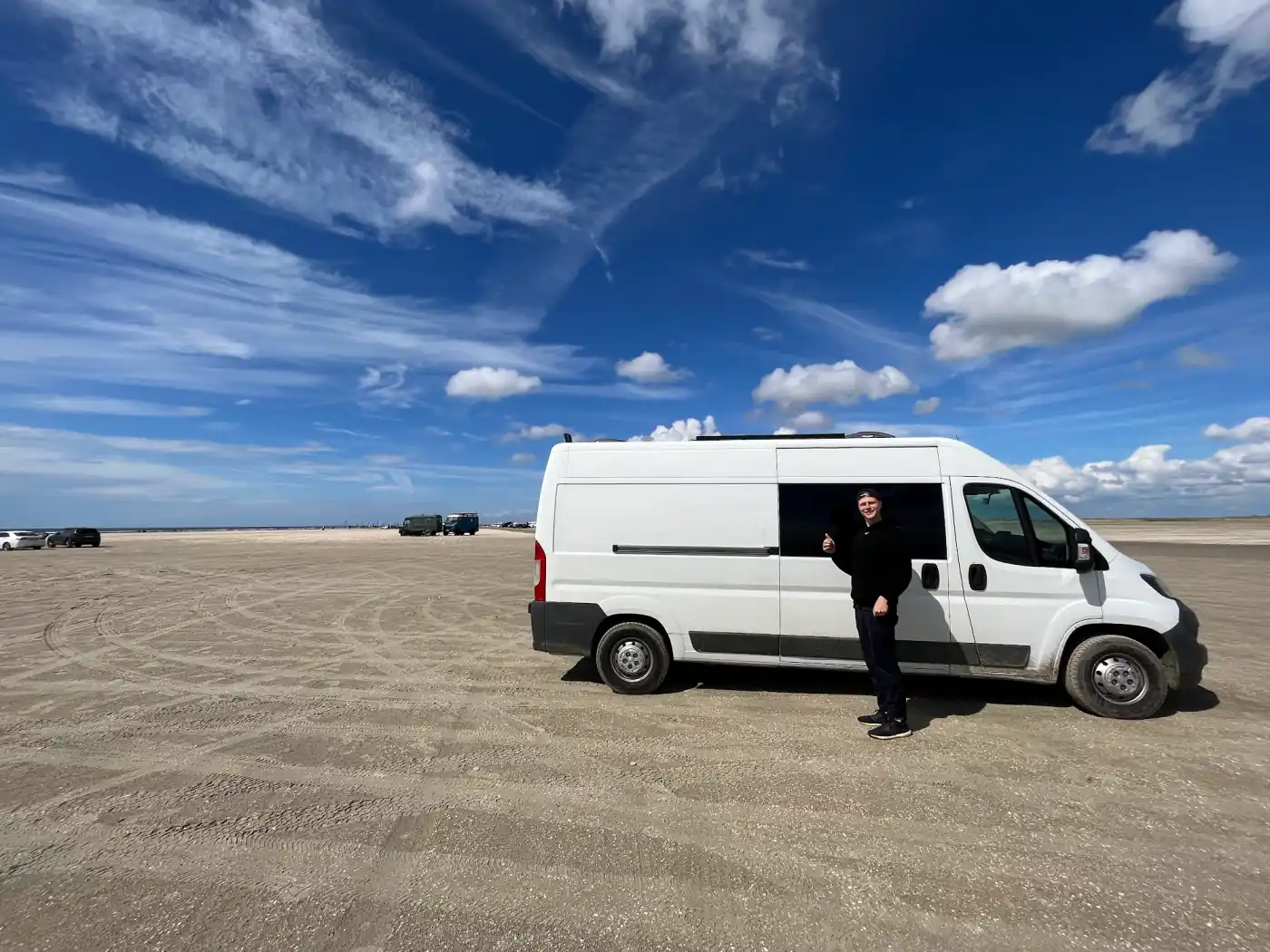 Mark neben dem weißen Kastenwagen von Lehmann Vlogs auf dem Strand von Rømø unter blauem Himmel