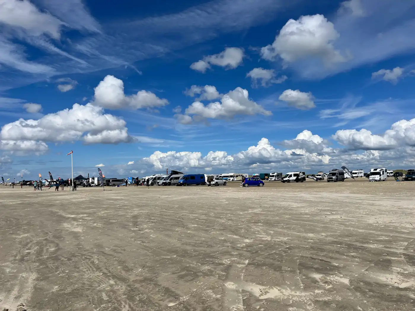 Lange Reihe geparkter Wohnmobile und Strandsegler-Flaggen auf dem breiten Strand von Rømø