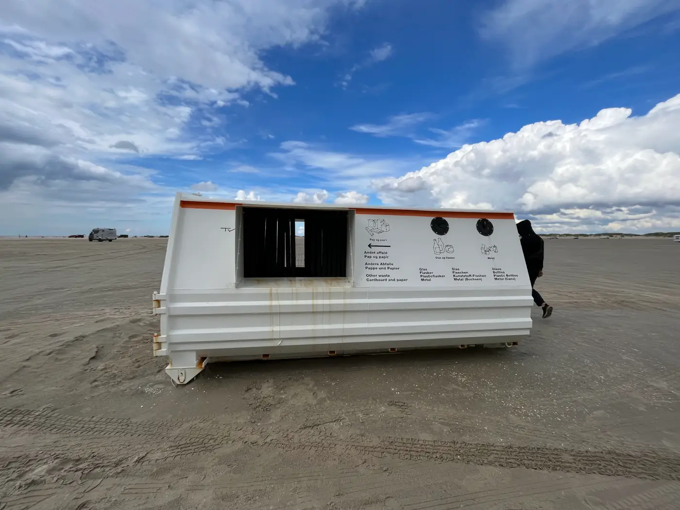 Weißer Müllcontainer mit mehrsprachiger Beschriftung mitten auf dem Strand von Rømø