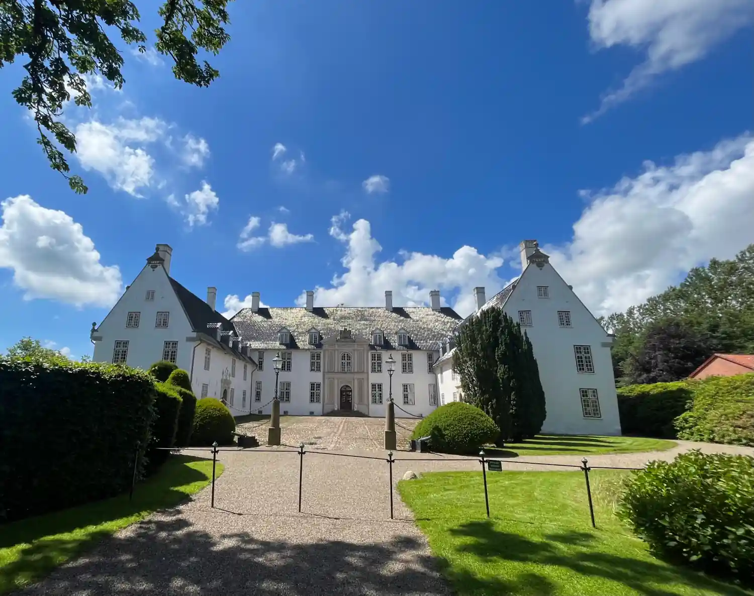 Weiße Fassade von Schloss Schackenborg in Møgeltønder mit Kieszufahrt und Hecken