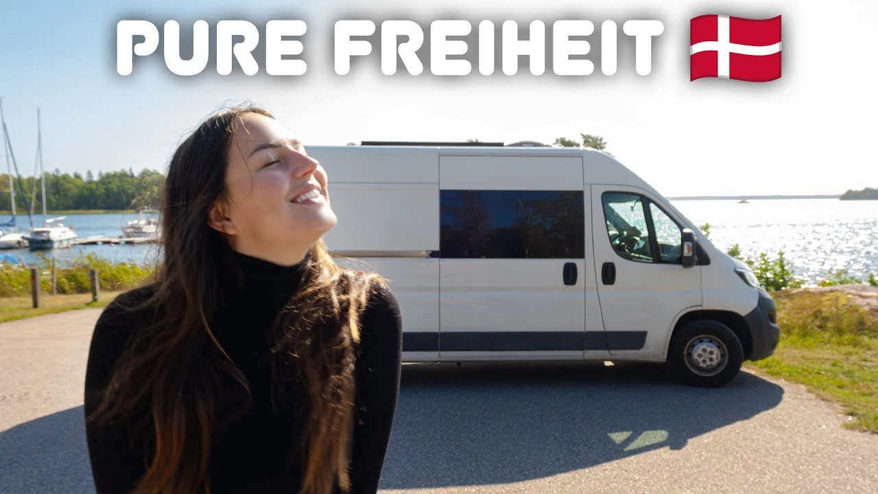 Lara von Lehmann Vlogs vor dem weißen Kastenwagen am Wasser, Vorschaubild unseres Videos zum Freistehen in Dänemark