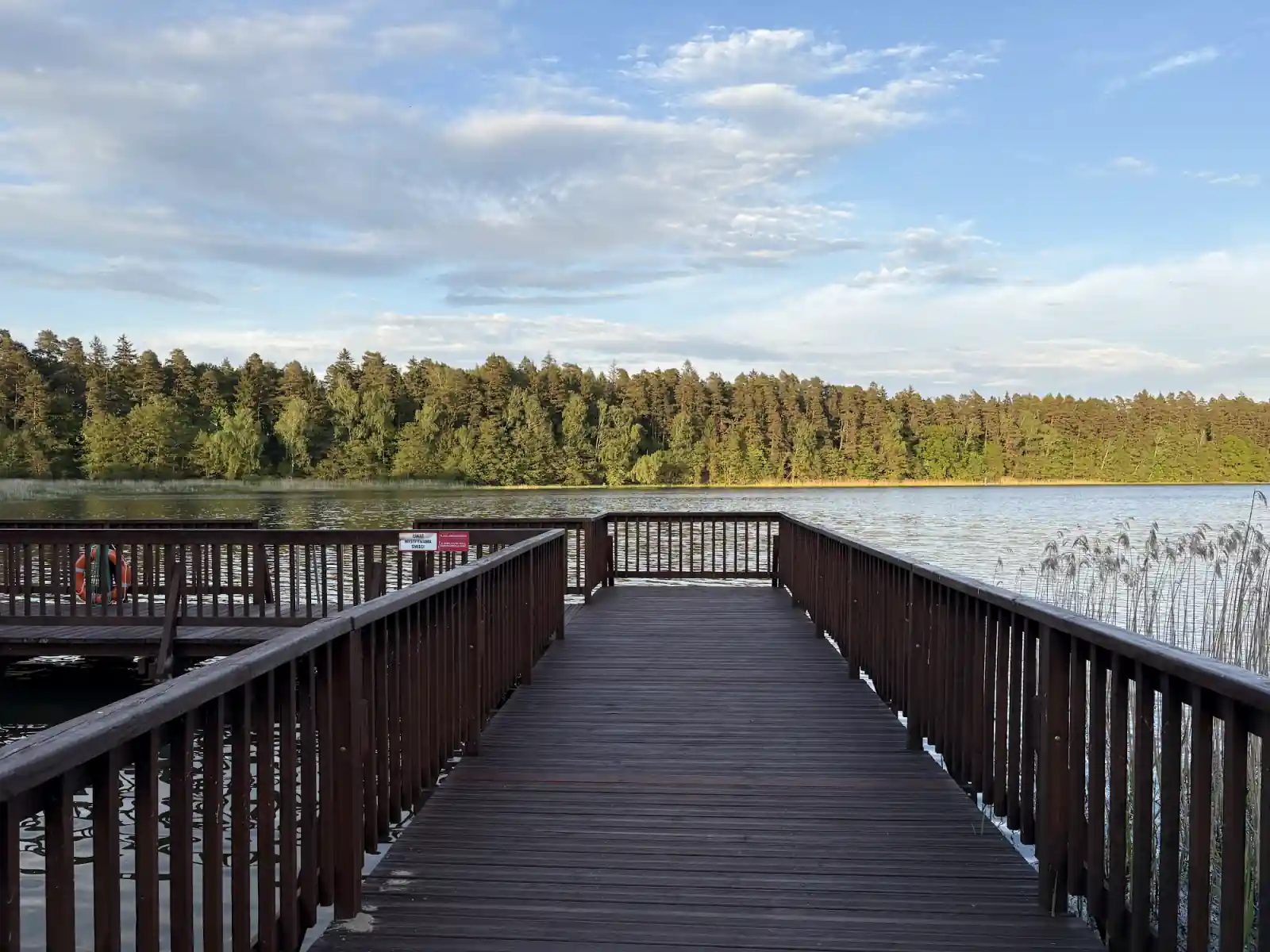 Holzsteg am Masurensee mit Blick auf Kiefernwald, Anfahrt nach Masuren mit dem Wohnmobil