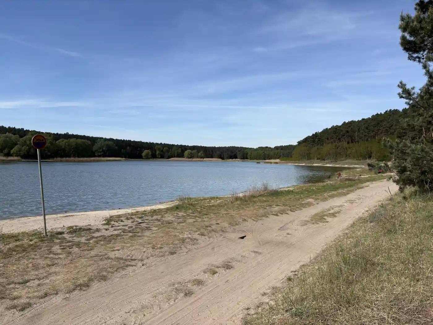Waldsee in Polen mit Sandufer und einem Badeverbotsschild am Ufer