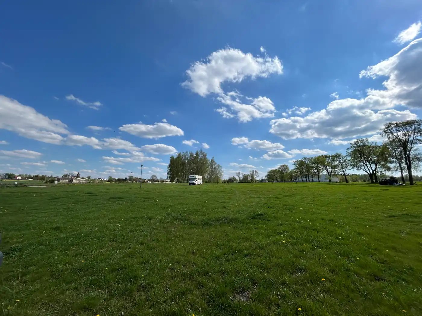 Weite Wiese in Polen unter blauem Himmel, im Hintergrund ein Wohnmobil und ein Auto
