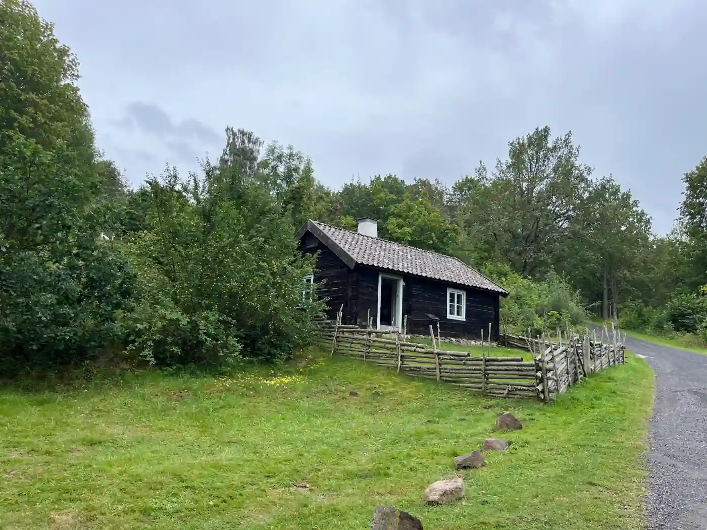 Dunkle Holzhütte mit Ziegeldach und Holzzaun im Freilichtmuseum auf dem Grännaberget