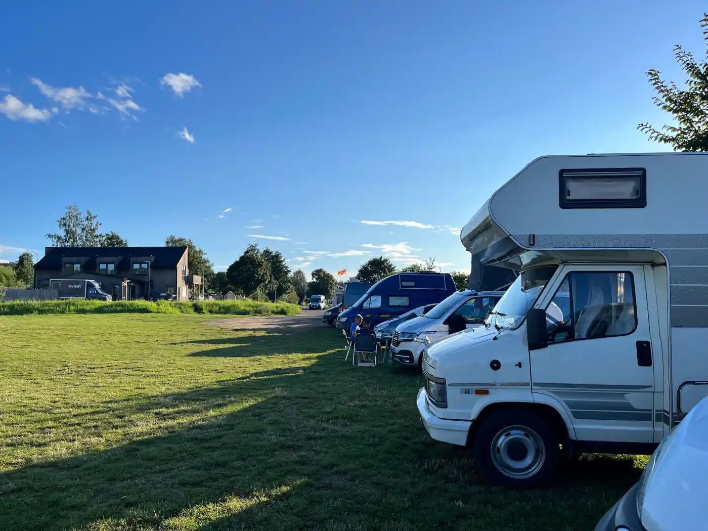 Mehrere Wohnmobile stehen abends auf einer Wiese an einem Badesee in Schweden