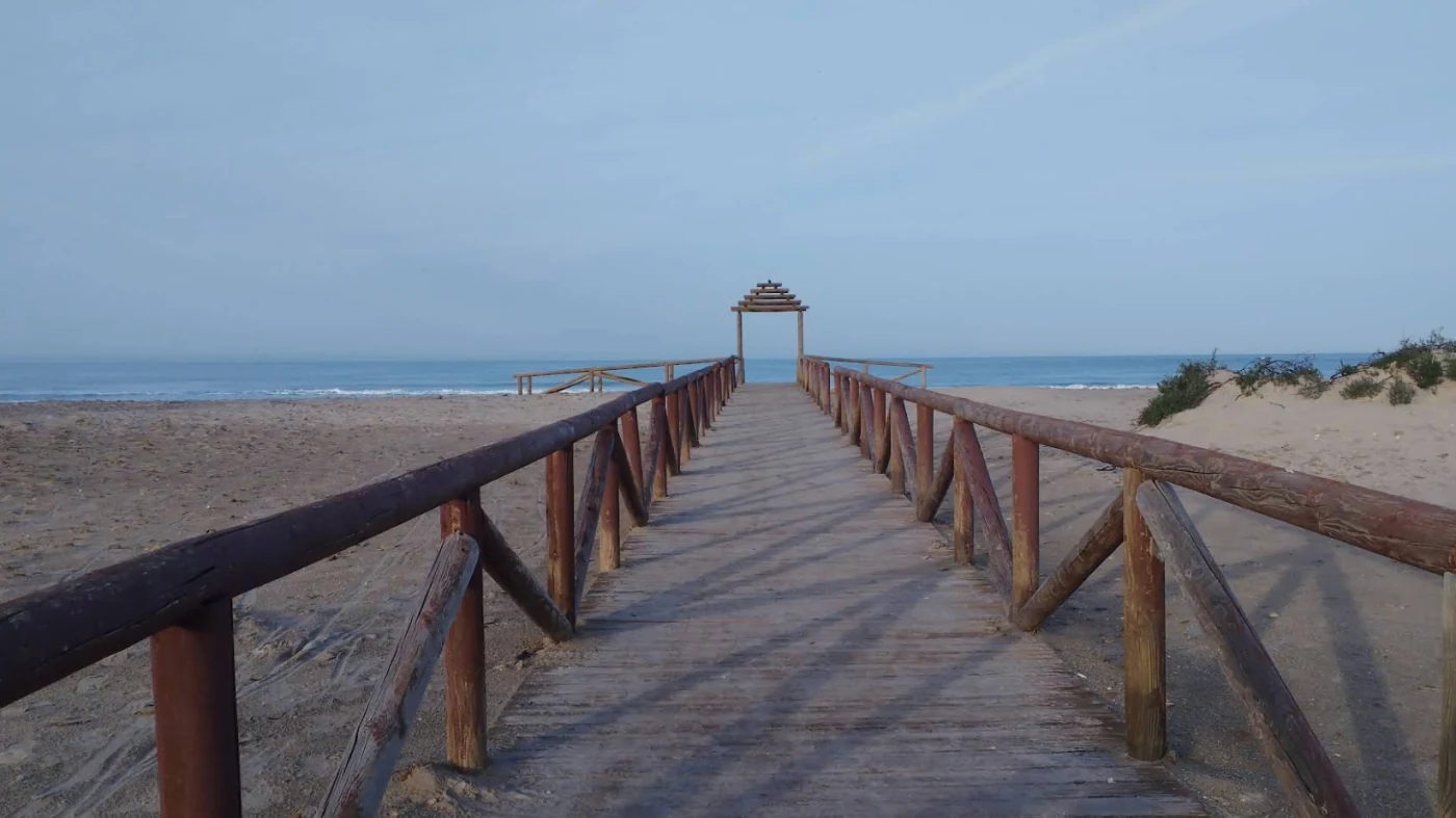 Hölzerner Steg über Dünen zu einem weiten leeren Sandstrand an der Costa de la Luz