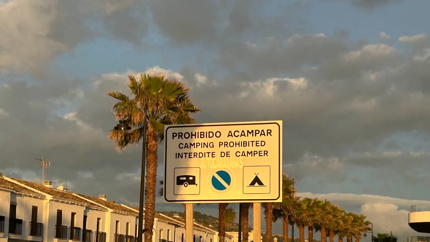 Gelbes Schild an einer andalusischen Strandpromenade mit der Aufschrift Prohibido acampar, Camping prohibited, Interdite de camper