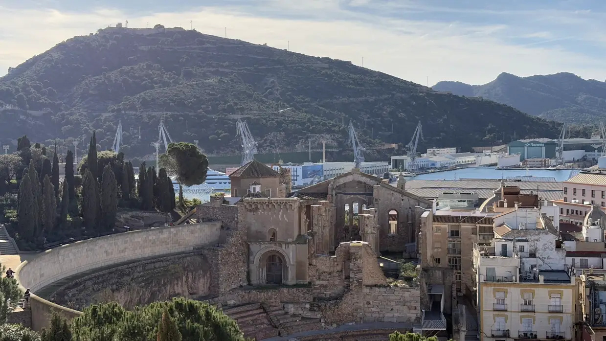 Das römische Theater von Cartagena von oben, daneben die Ruine der Kirche Santa María, im Hintergrund Hafenkräne und ein bewaldeter Berg