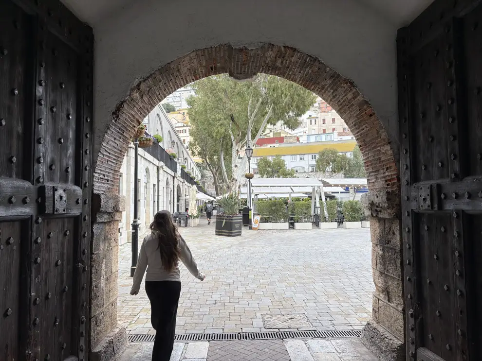 Lara von Lehmann Vlogs geht durch ein altes Festungstor mit schweren Holztüren auf den Grand Casemates Square in Gibraltar