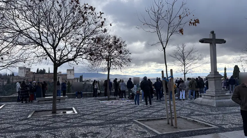 Viele Besucher auf dem gepflasterten Platz des Mirador de San Nicolás in Granada, links im Hintergrund die Türme der Alhambra unter Wolken