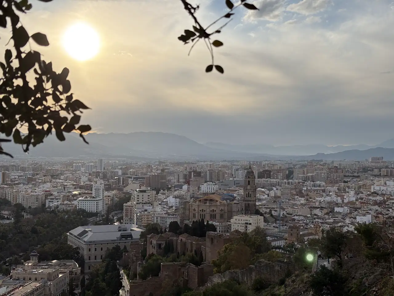 Blick von den Mauern des Castillo de Gibralfaro über die Dächer von Málaga mit dem Turm der Kathedrale, darüber die tief stehende Sonne