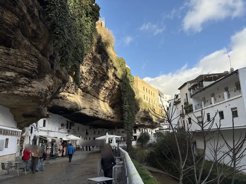 Gasse in Setenil de las Bodegas unter einem riesigen Felsüberhang, darunter weiße Häuser, Läden und Sonnenschirme