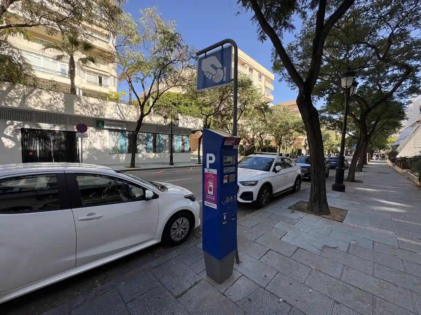 Parkautomat einer blauen Zone an einer Straße in Spanien mit parkenden Autos und Palmen