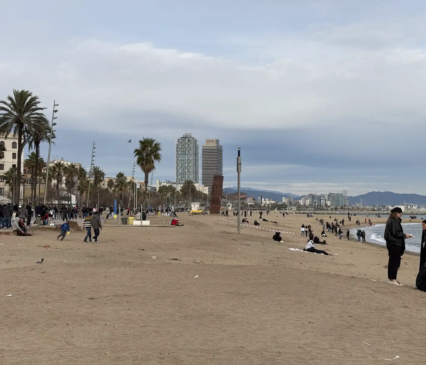 Breiter Sandstrand der Barceloneta in Barcelona mit Hochhäusern und Bergen im Hintergrund
