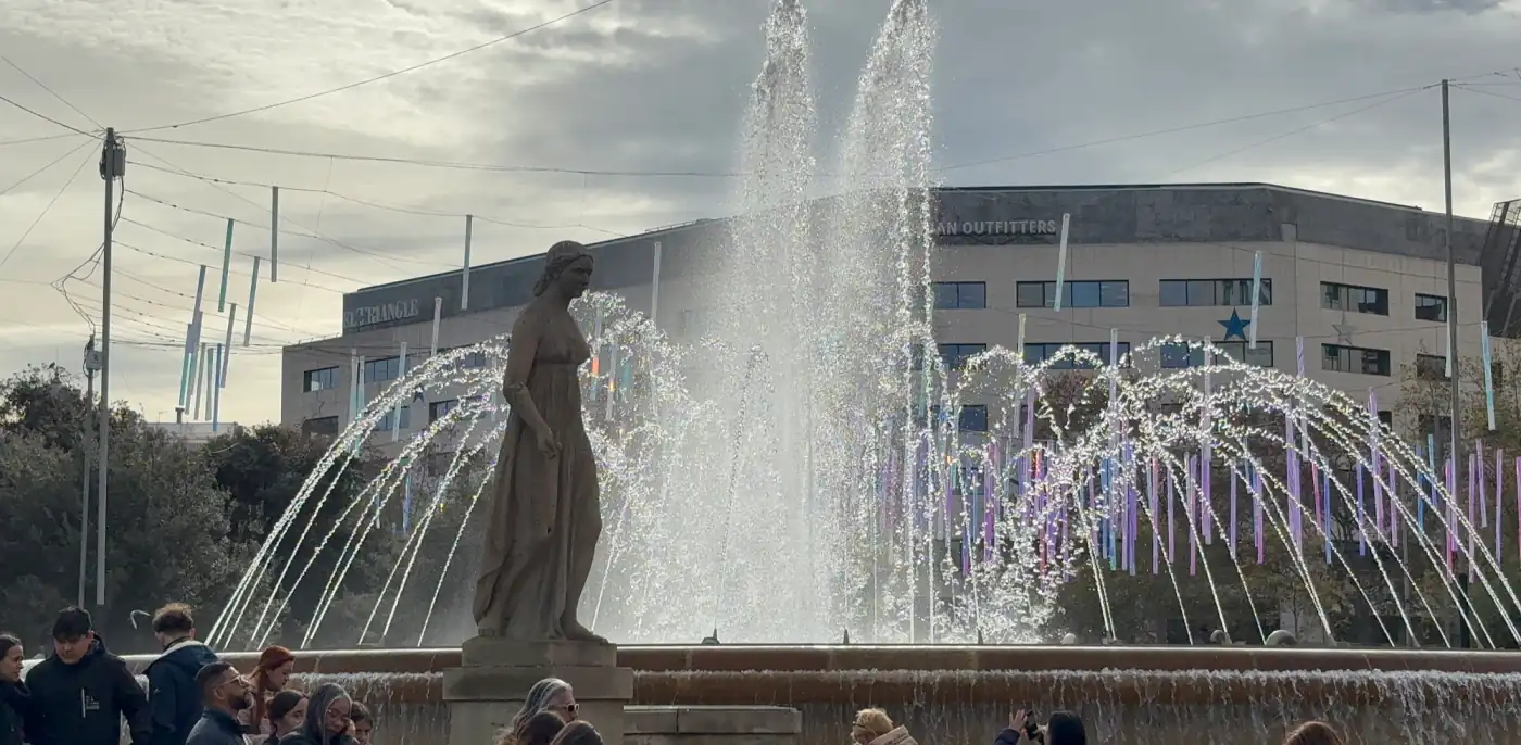 Brunnen mit Statue an der Plaça de Catalunya in Barcelona, dahinter Kaufhäuser