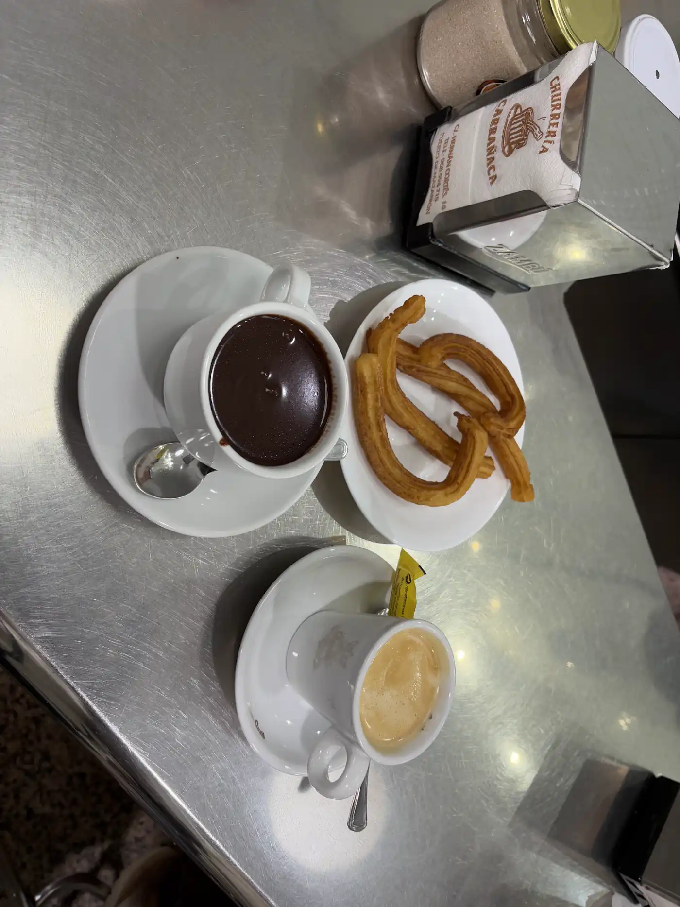 Churros mit dicker heißer Schokolade und einem Kaffee auf einem Edelstahltresen