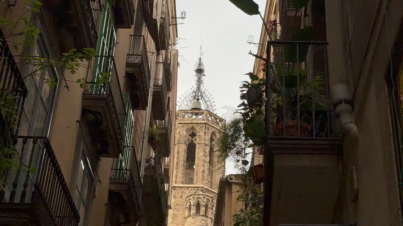 Gotischer Kirchturm zwischen engen Häuserfassaden mit Balkonen im Gotischen Viertel von Barcelona