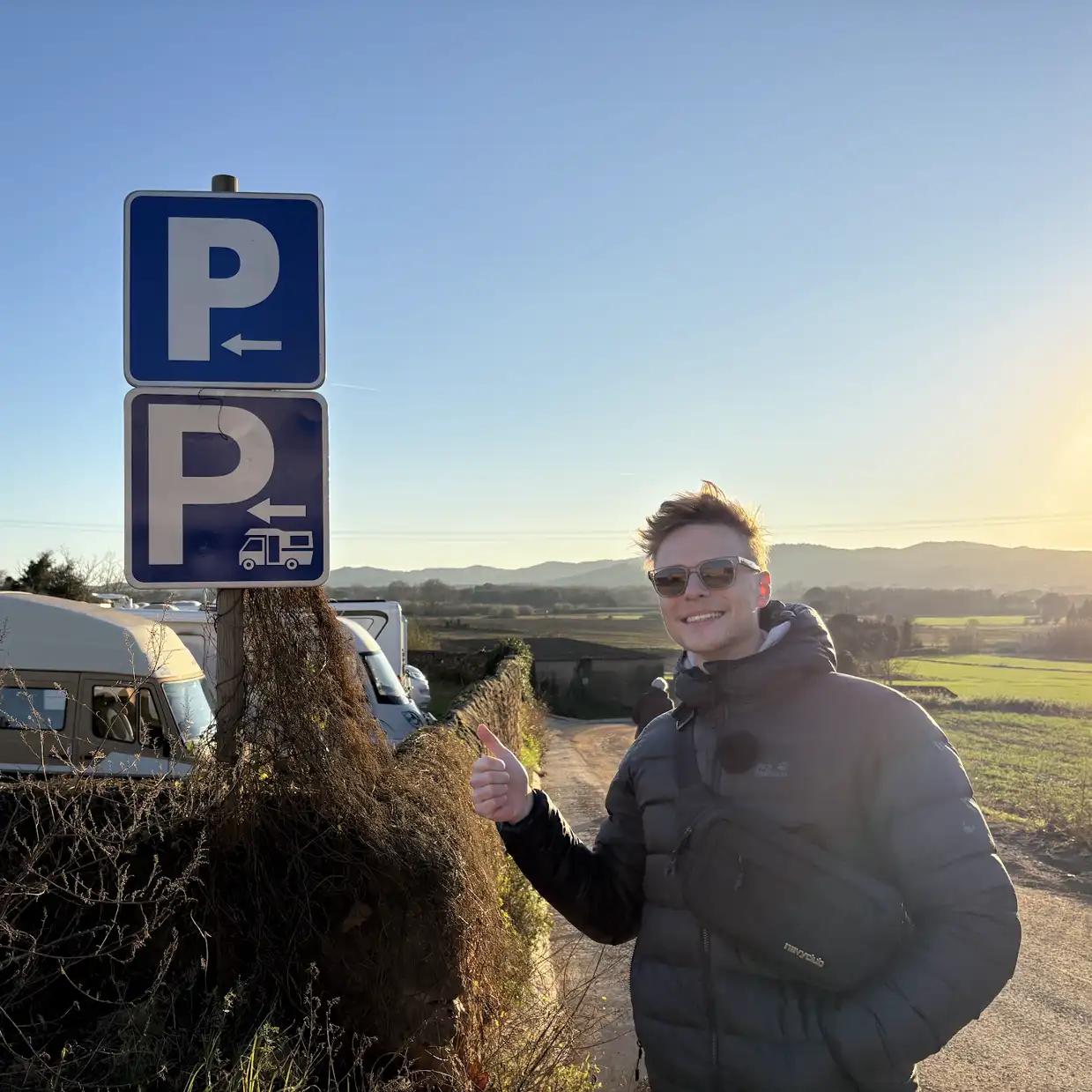 Mark zeigt den Daumen hoch neben einem Parkschild mit Wohnmobil-Symbol am Ortsrand von Pals