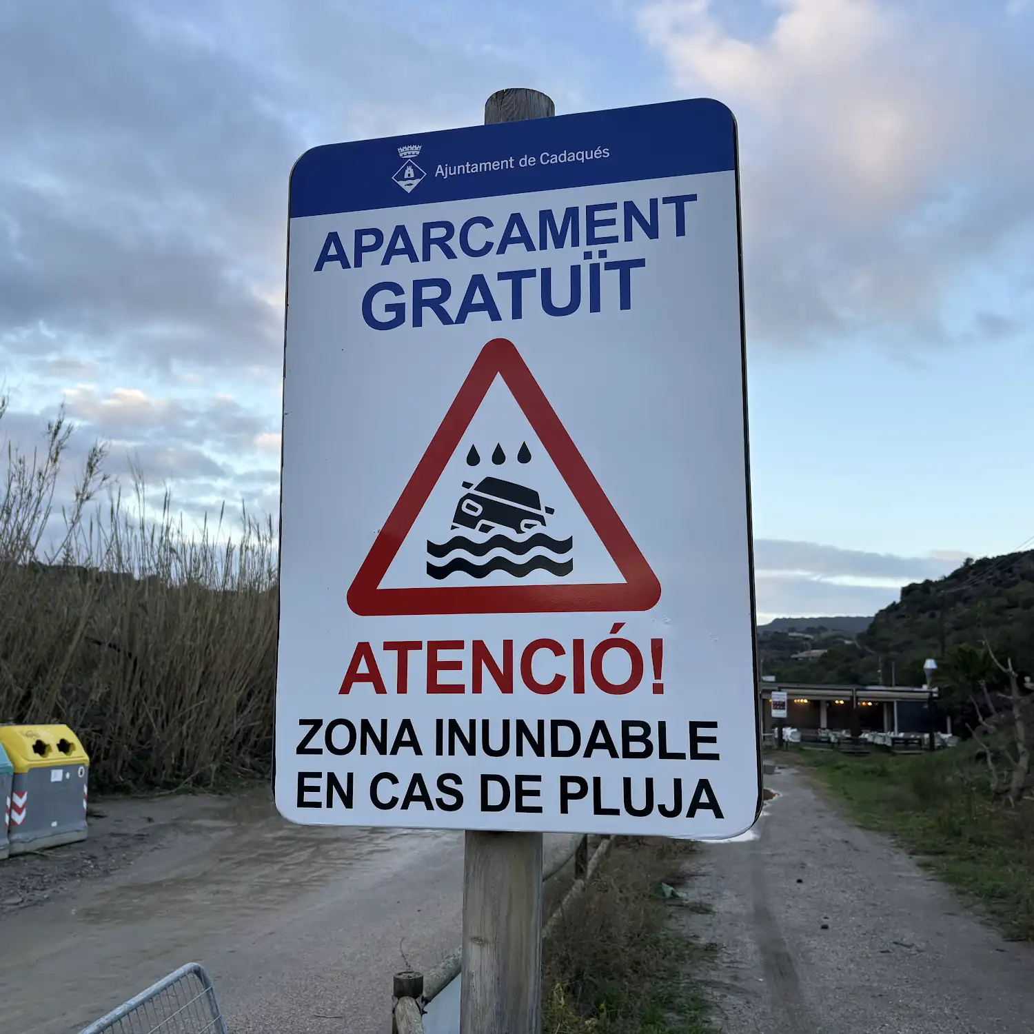 Schild der Gemeinde Cadaqués am Parkplatz Portlligat: kostenloses Parken und Warnung vor Überflutung bei Regen