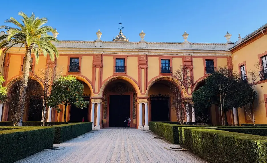 Innenhof des Alcázar von Sevilla mit Arkaden, Hecken und gelb-rot gestrichener Fassade