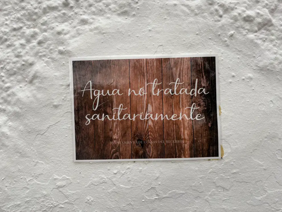Schild mit der Aufschrift Agua no tratada sanitariamente an einer weißen Wand an einem Platz mit Quelle in Andalusien