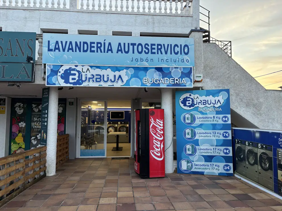 Eingang eines Selbstbedienungs-Waschsalons an der Costa Brava mit Preistafel für Waschmaschinen nach Kilogramm und dem Hinweis, dass Waschmittel inklusive ist